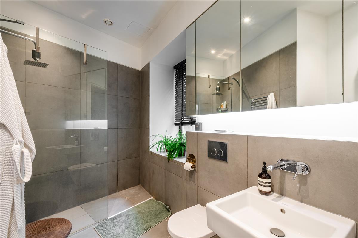 En-suite Bathroom - Set within a beautifully reimagined Victorian warehouse in the heart of Clerkenwell, this exceptional two-bedroom apartment combines industrial heritage with contemporary refinement. Occupying part of a thoughtfully converted late-19th-century building, the apartment extends to an impressive 1,368 sq ft, with soaring ceilings exceeding three metres, expansive factory-style glazing and carefully considered interiors throughout.