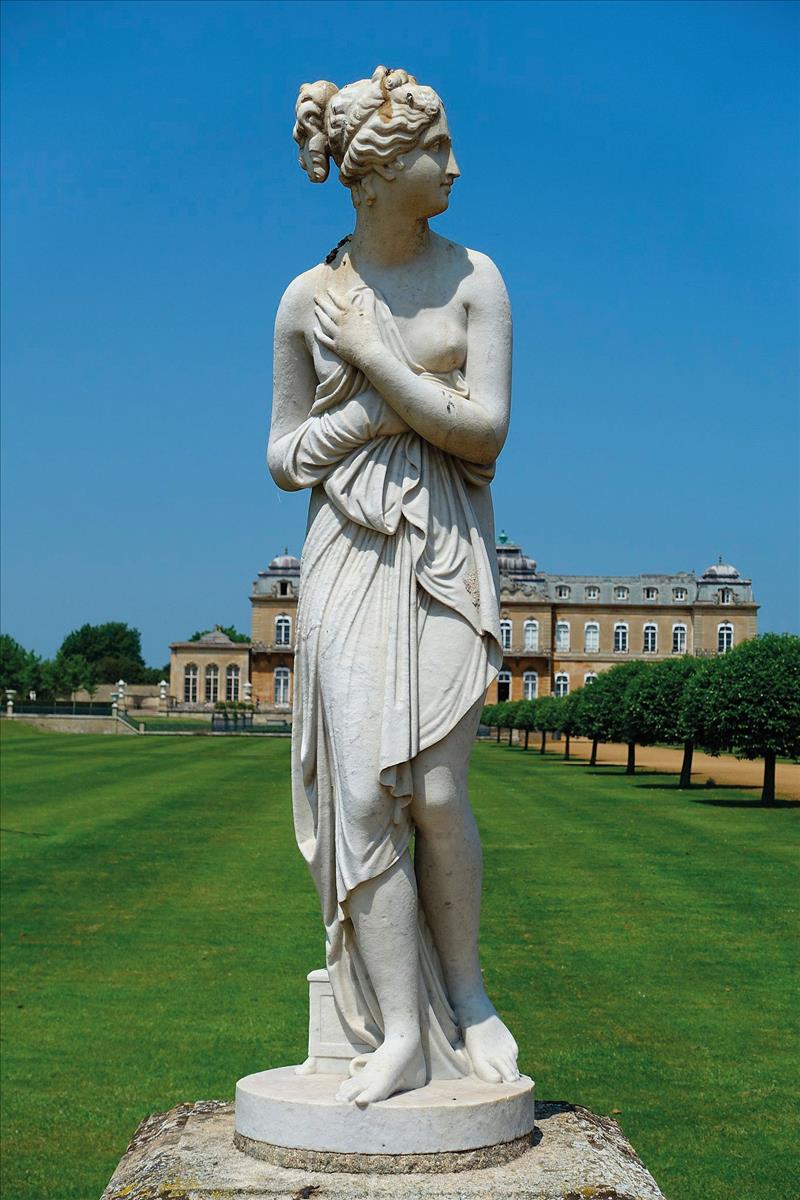 garden statue infront of lawn trees and stately home